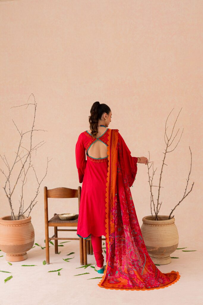 a woman in a red dress standing in front of a potted plant.